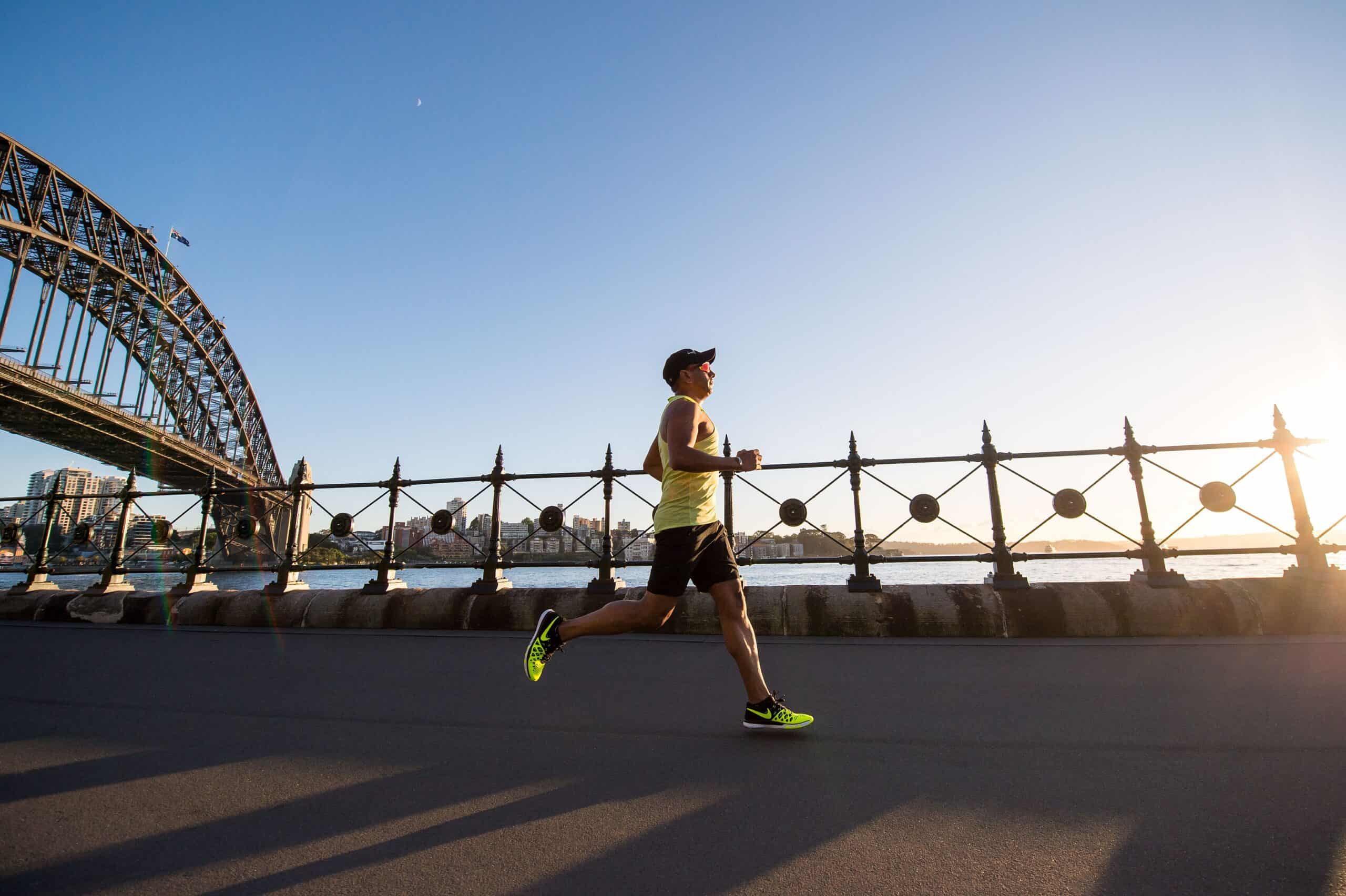 Man dressed in bright yellow runs beneath a bridge.

