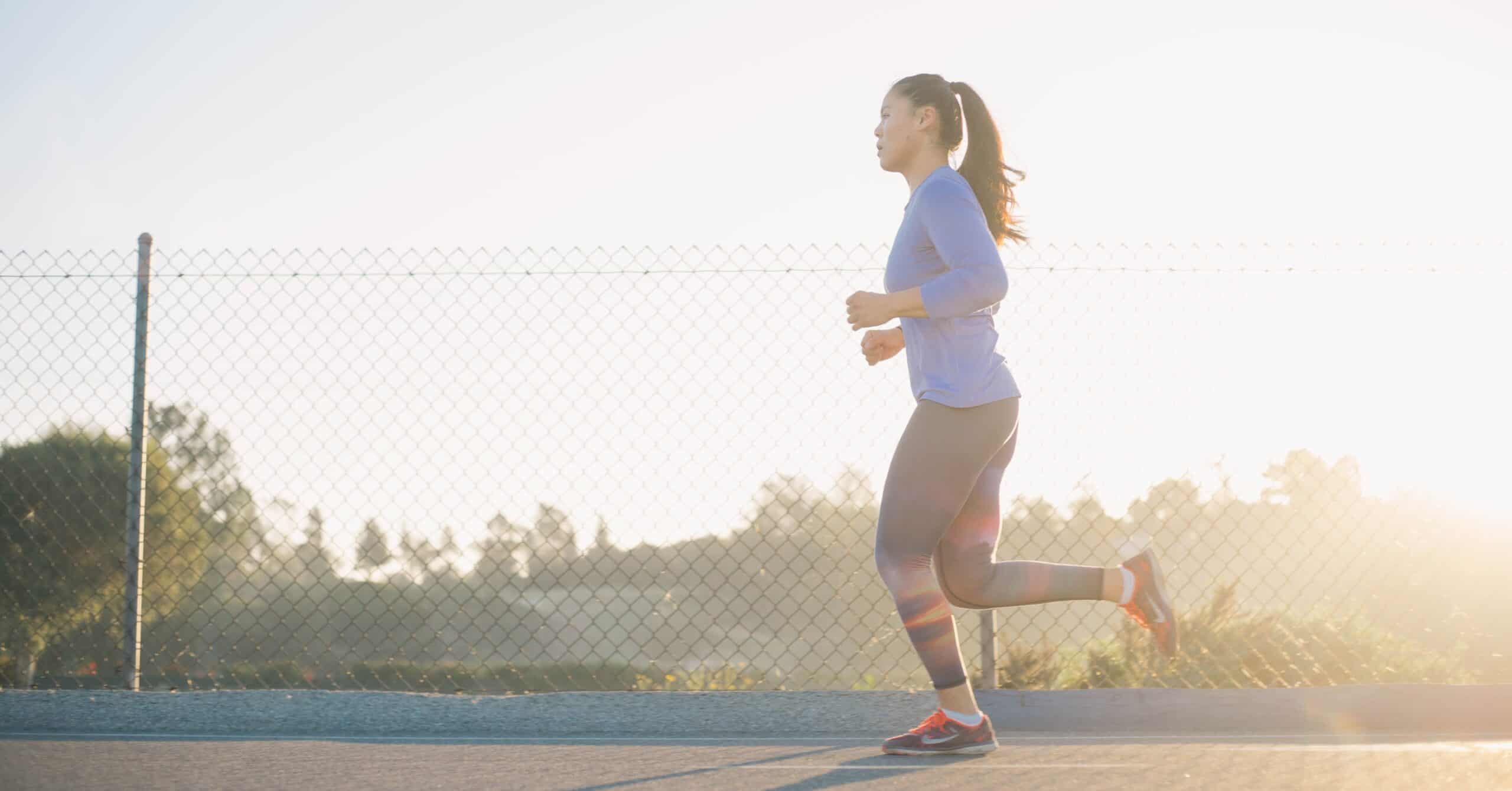 A woman running with correct running posture with her foot landing underneath her flexed knee and an upright open core and chest.