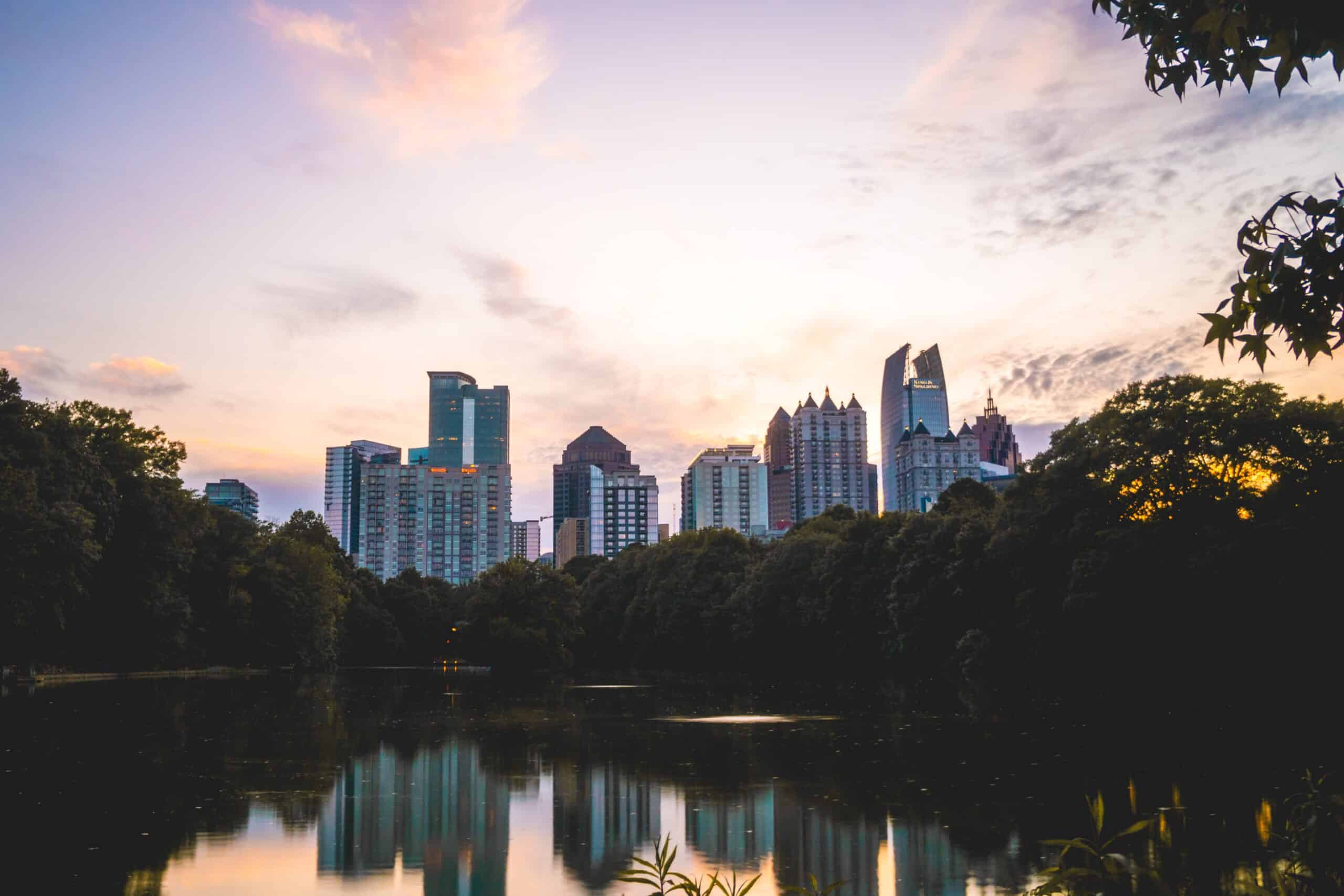 A view of the Atlanta skyline from a pond in Piedmont Park at dusk.