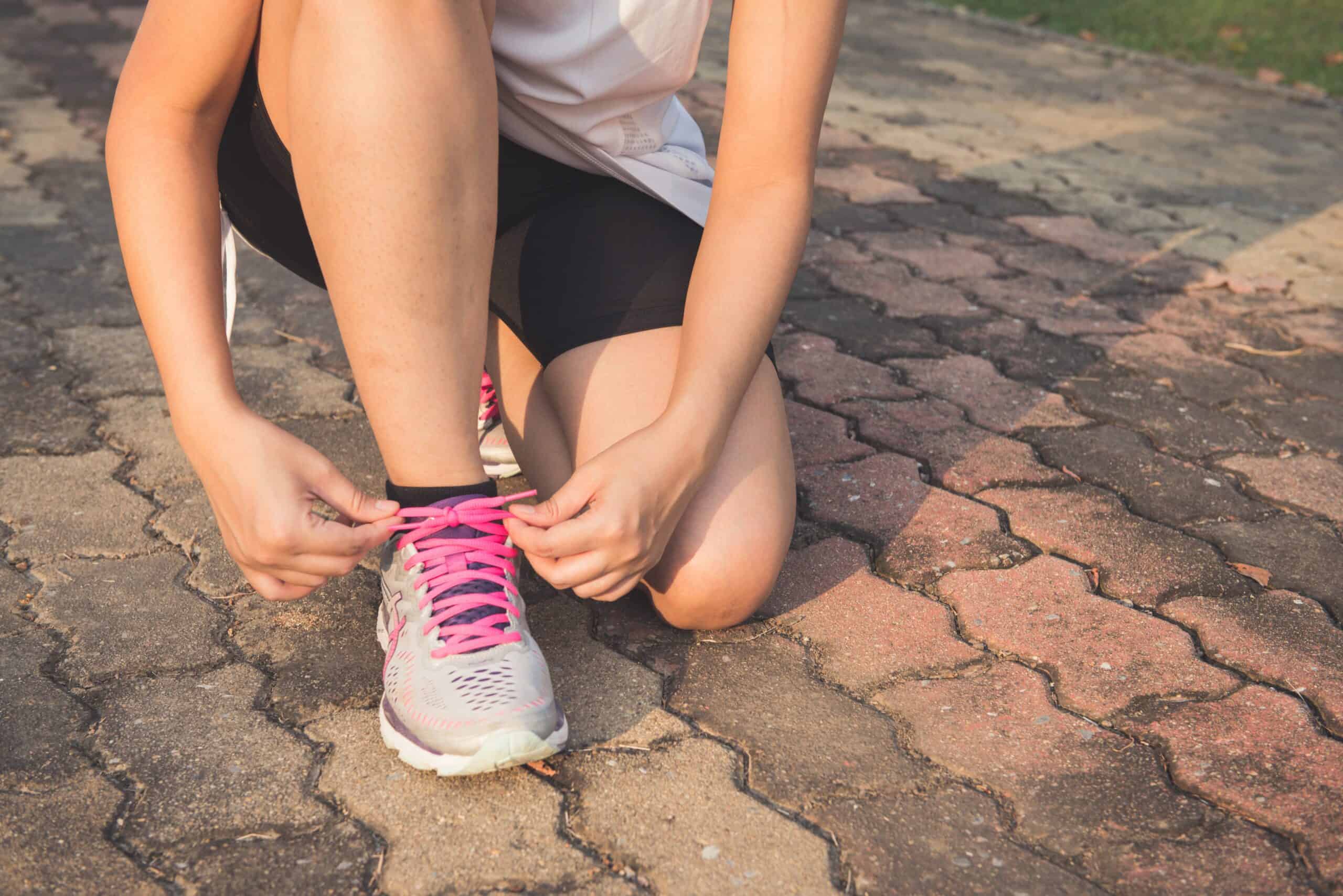 Gear is the first item to consider when running on a budget - girl tying her shoes.