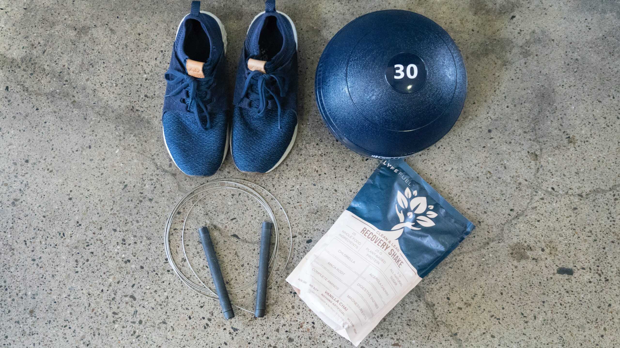 Workout shoes, a 30kg weight ball, a speed rope and creatine for runners against a concrete floor.