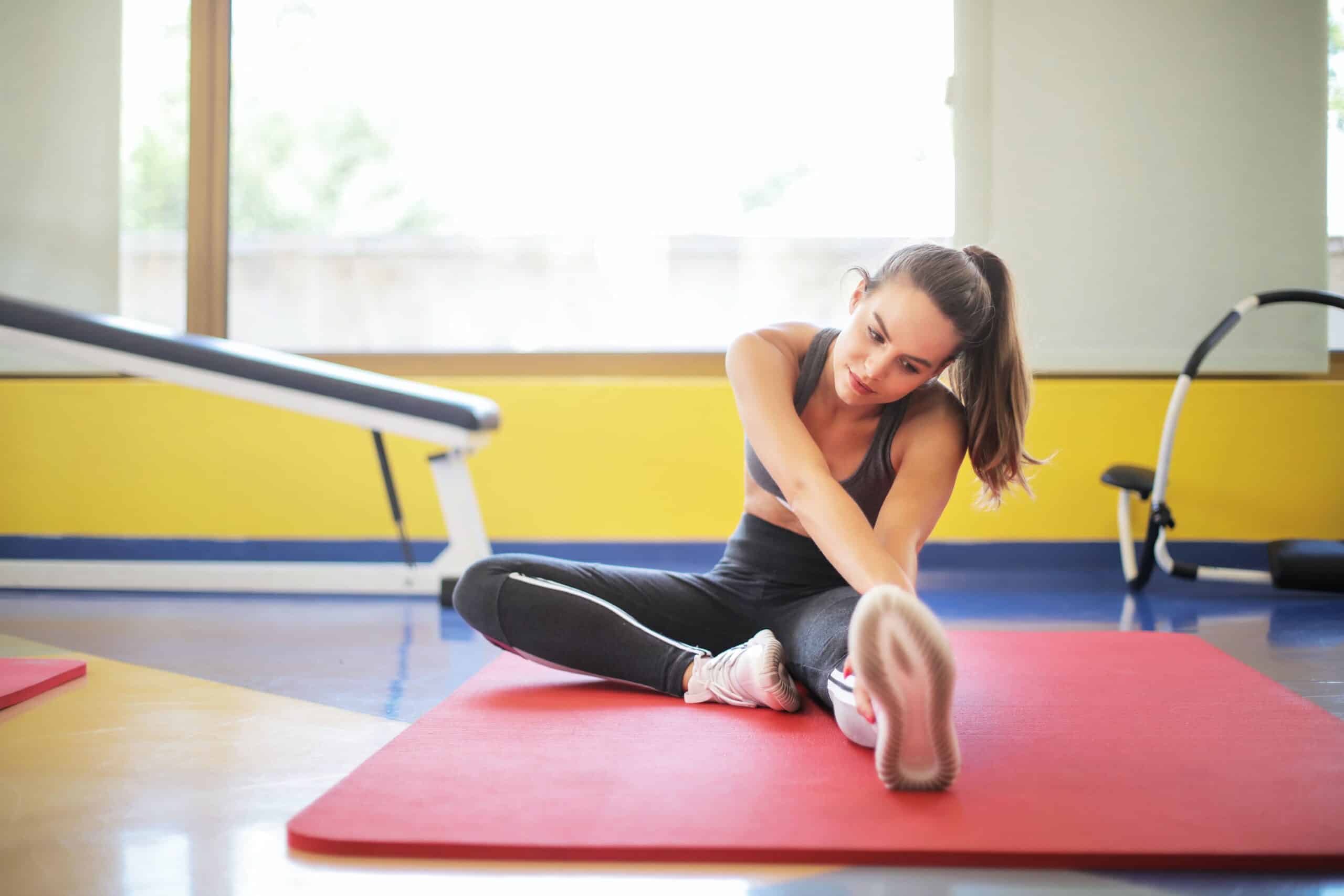 A woman stretching in a gym as part of running recovery.