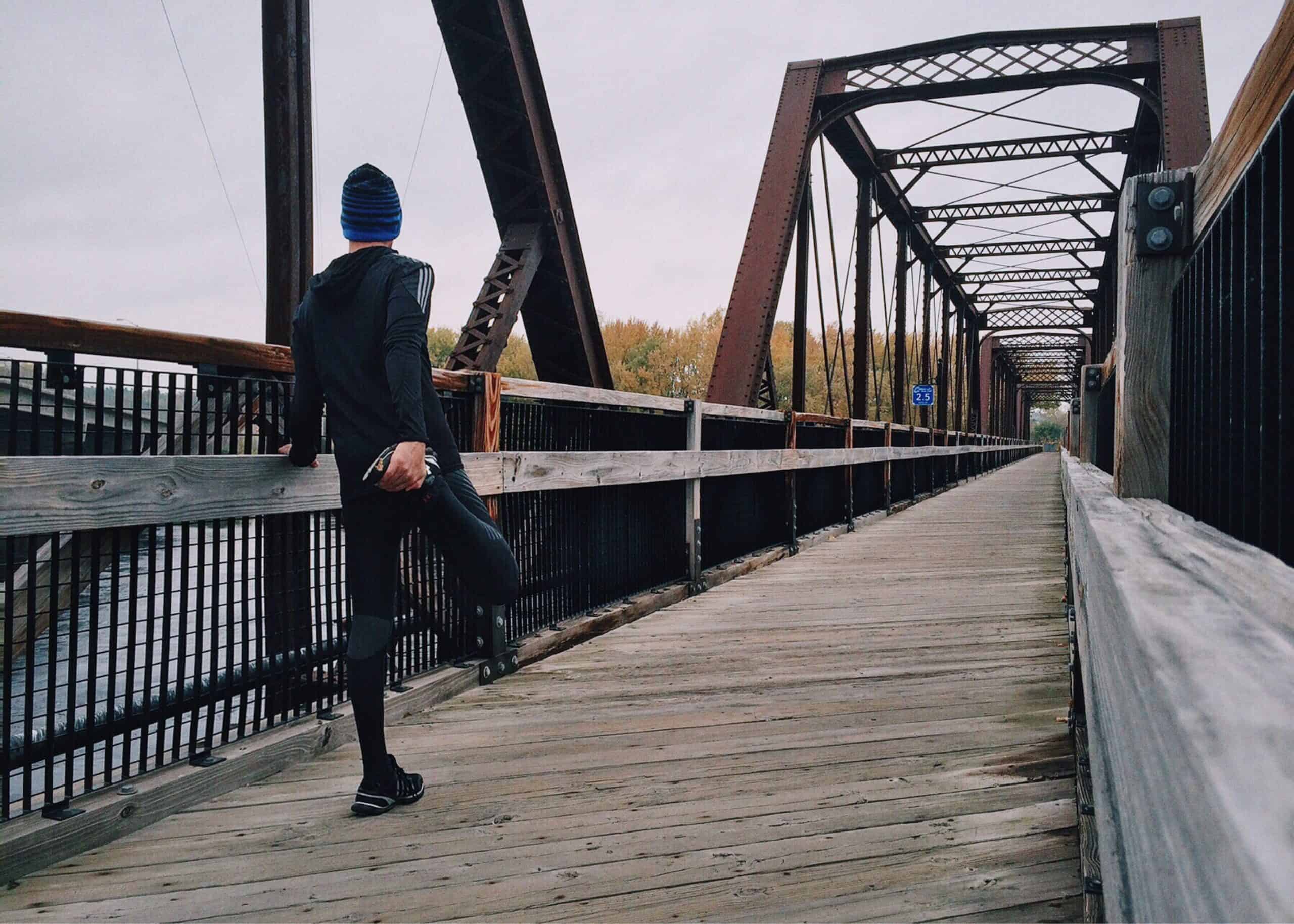 Can you run a marathon without training - a man on a bridge stretching his quad before a run. 