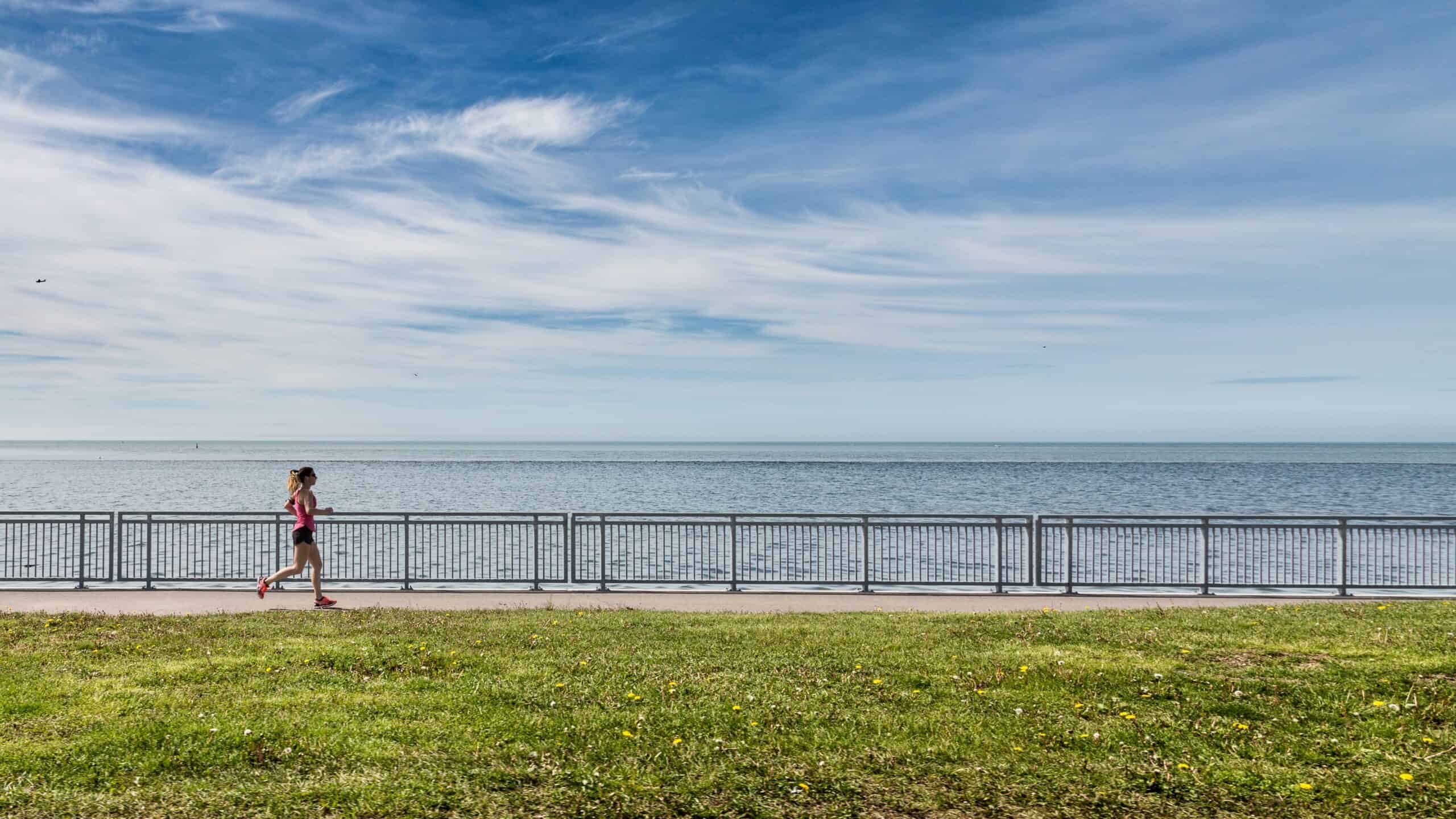 A woman running on a sidewalk next to a body of water.