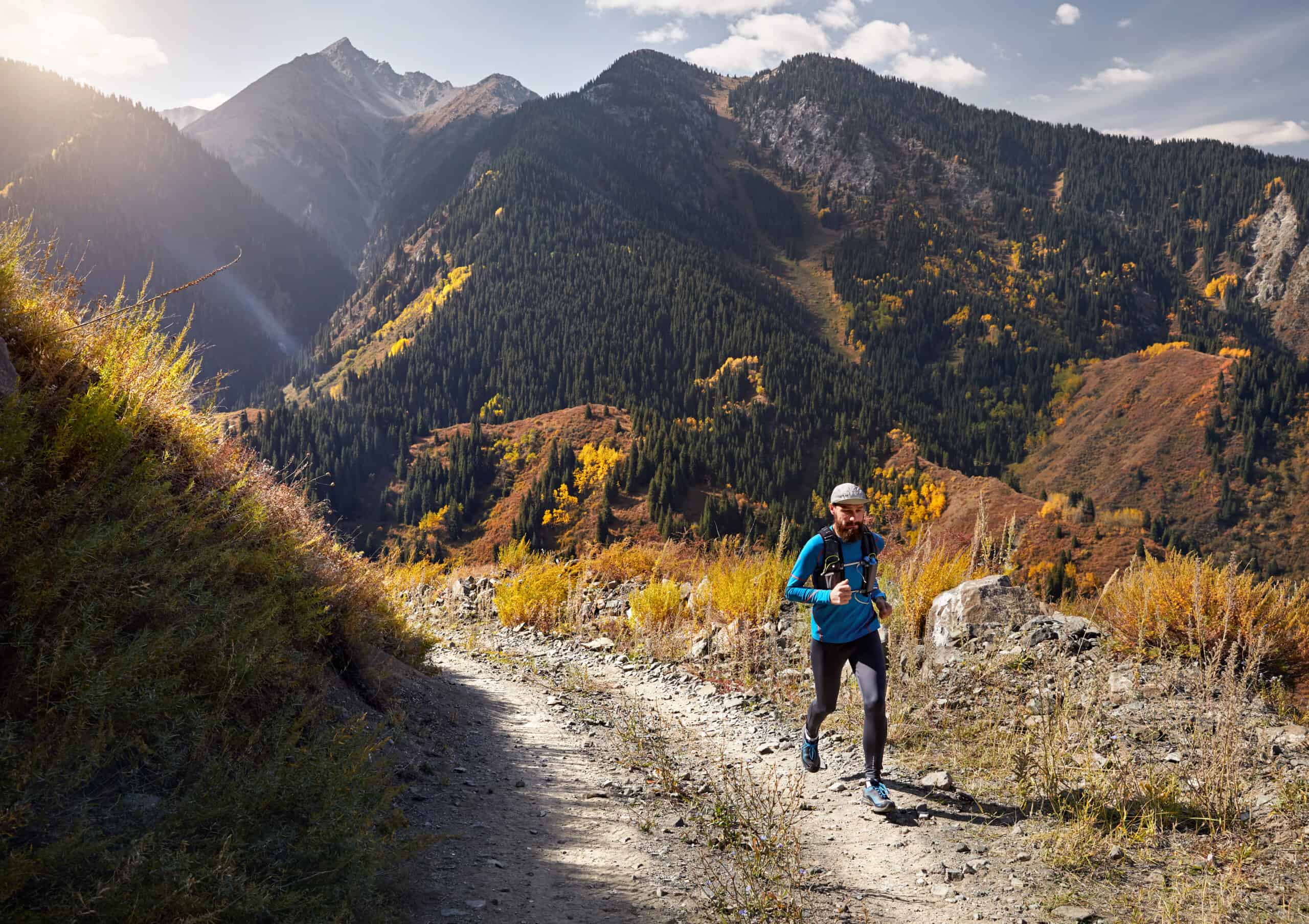 Runner athlete with beard running on the trail in the mountains who has learned how to start trail running.