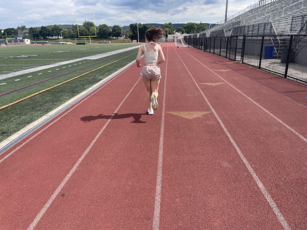 Our writer and gear tester running in the Saucony Hurricane 24 on a high school track with her back toward the camera.
