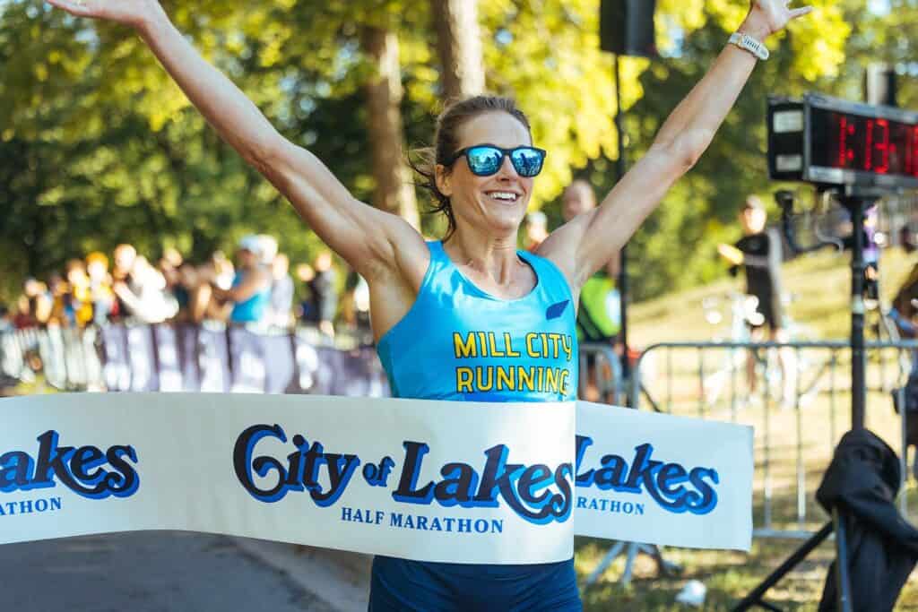 woman runner crossing finish line of the City of Lakes Half Marathon